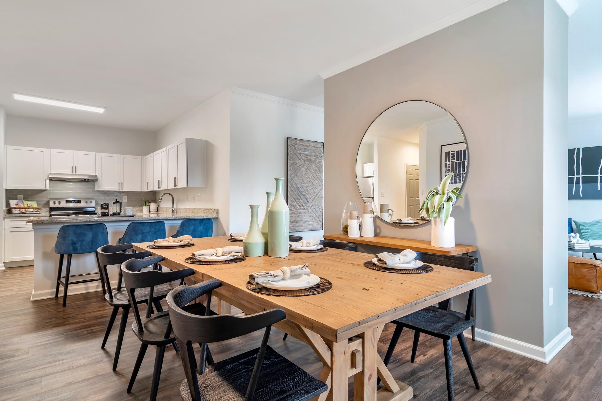 Model dining room with large table and breakfast bar seating looking into the kitchen