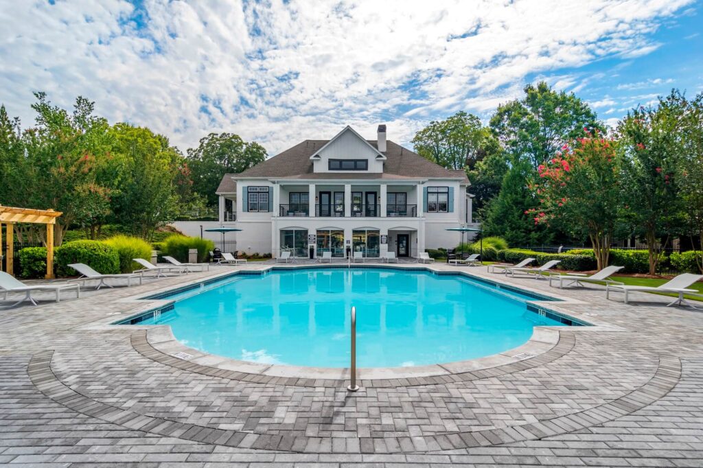 Wide shot of the pool, deck seating, and surrounding landscaping, looking towards the clubhouse