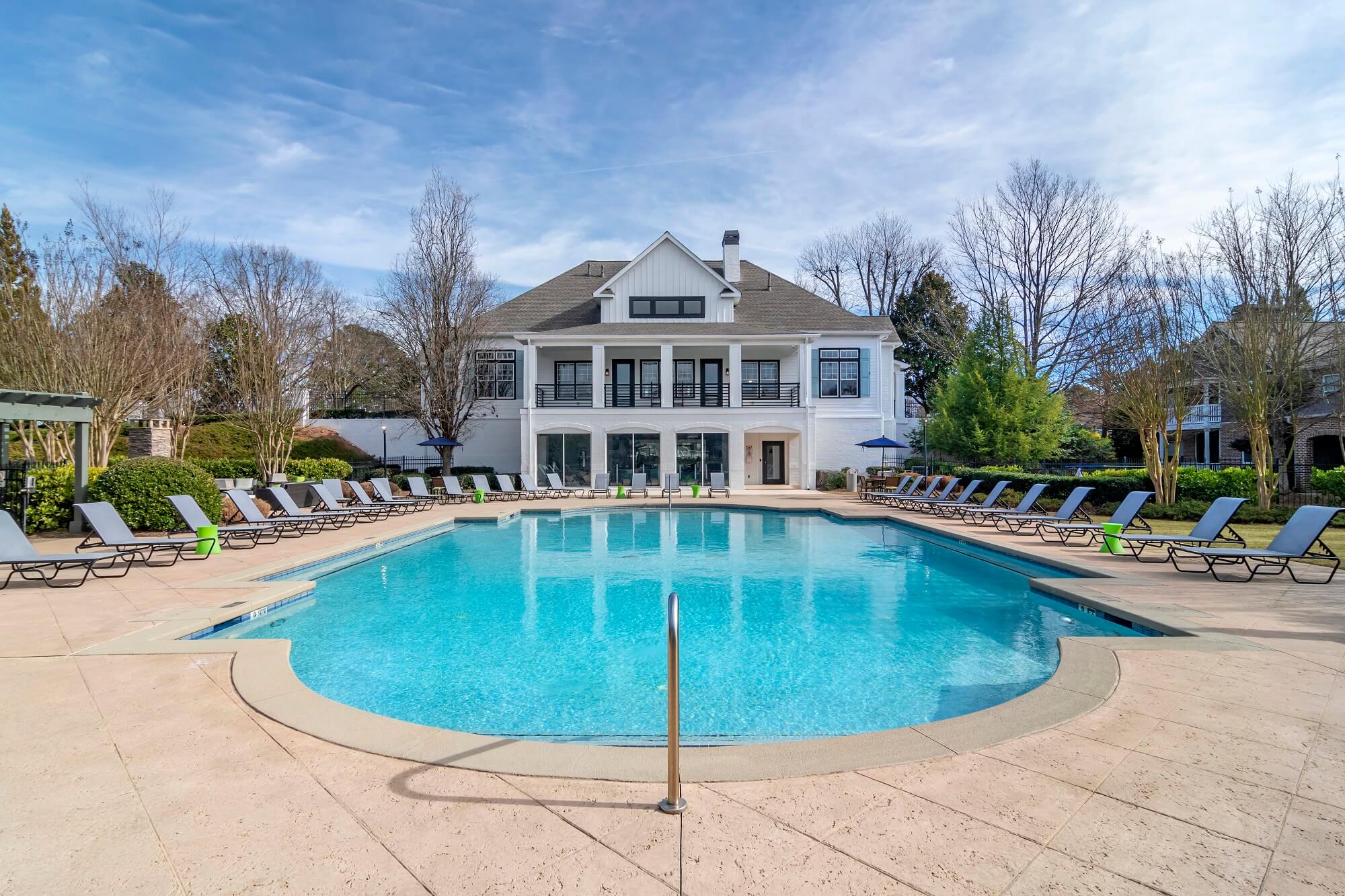 Wide shot of the pool, deck seating, and surrounding landscaping, looking towards the clubhouse